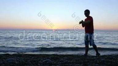 日落时分，一个男人的剪影带着一只智能手表沿着水边经过。 他停下来，查看智能手表上的信息